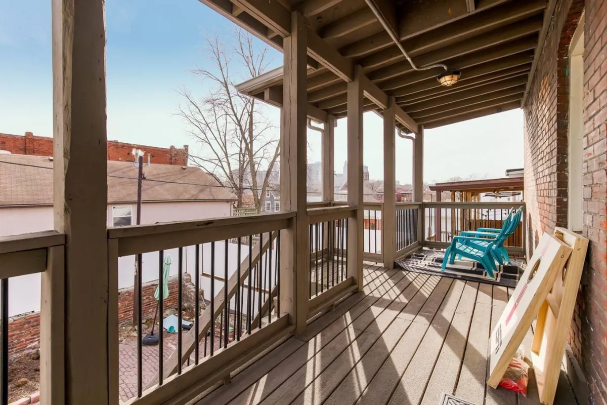 An inviting exterior seating area with blue chairs, wooden railing, and brick walls, set in an open space ideal for socializing or enjoying morning sunrises and evening relaxation.