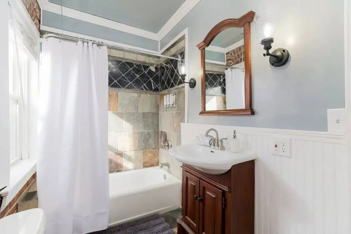 This image features a tranquil, well-appointed bathroom with a bathtub, vanity sink, mirror, and shower curtain. The serene atmosphere and clean design highlight the comfort and functionality of the bathroom space.