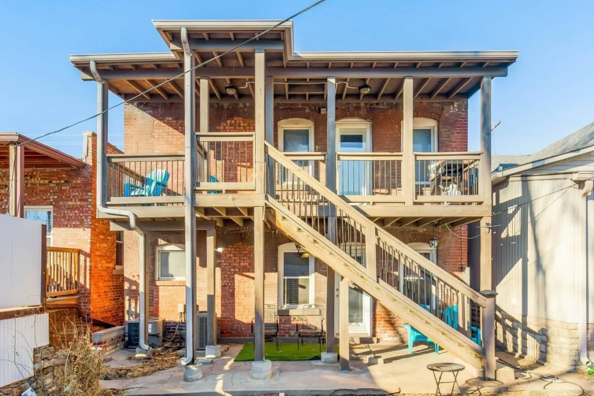 An exterior perspective showing a wooden staircase, multiple balconies, a classic brick facade, and outdoor seating areas. This lively communal space is ideal for family gatherings, barbecues, or relaxing after returning from local adventures.