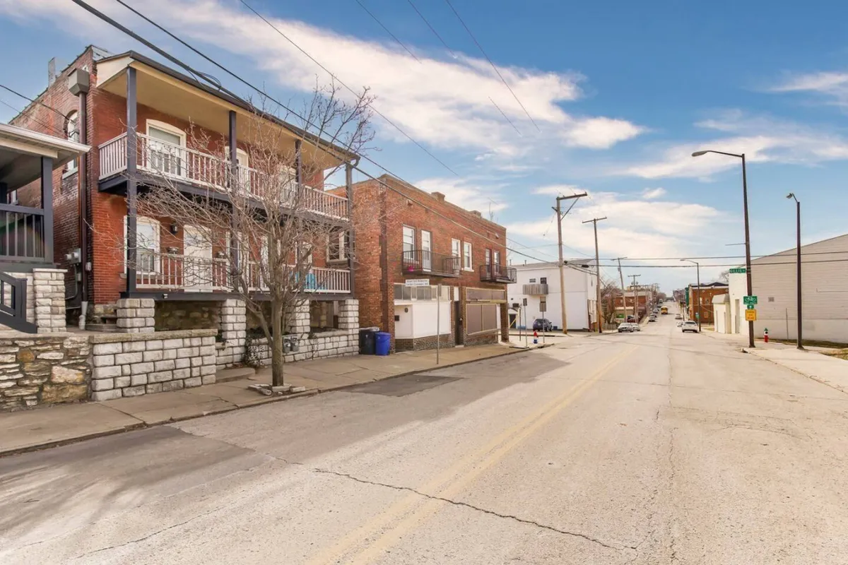 A friendly streetscape featuring two-story brick buildings, leafy street trees, and wide sidewalks, inviting guests to explore the local community by foot. The image hints at nearby shops and neighborhood activities, creating a sense of place.