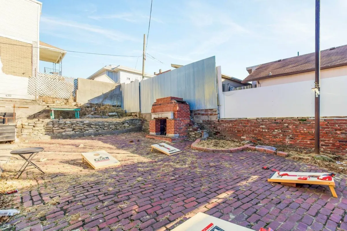 An inviting outdoor space featuring an outdoor fireplace, brick pathway, cornhole boards, and surrounding walls. The scene is set for lively gatherings, barbecues, and casual games, embodying the social, group-focused spirit described in the section.